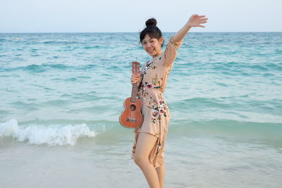 Portrait of smiling young woman standing at beach against sky during sunset