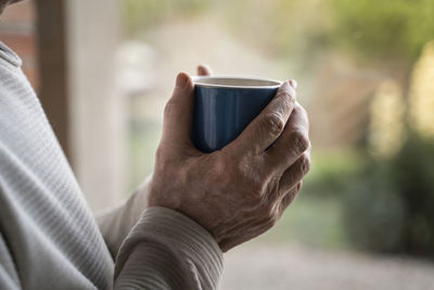 Close-up of man holding coffee cup while standing at home