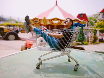 Man sitting in shopping cart on footpath