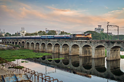 Bridge over river by city against sky during sunset