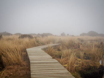 Boardwalk on field against clear sky