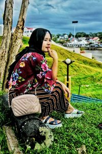 Woman sitting on log in city against sky