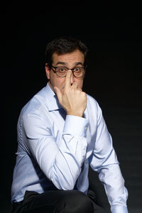 Portrait of young man sitting against black background