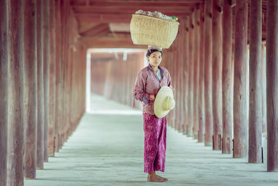 Portrait of woman carrying basket on head standing in corridor