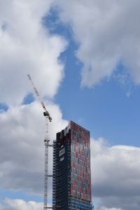 Low angle view of crane by building against sky