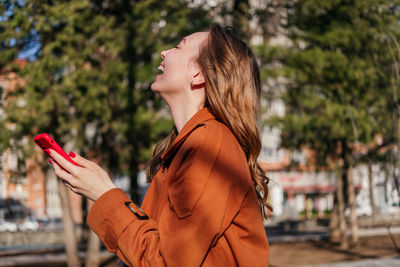 Laughing young woman holding smartphone in hand outdoors. girl having phone call on the street