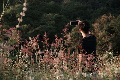 Rear view of man taking selfie with mobile phone by plants