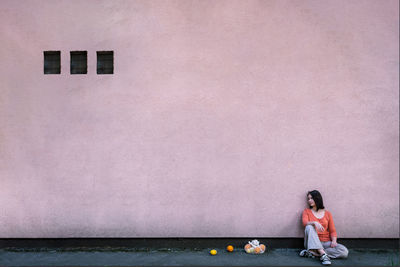 Side view of woman sitting against pink wall