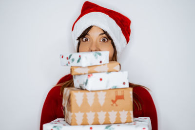 Portrait of smiling woman holding christmas gifts while standing against white background