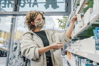 Female customer wearing protective face mask while checking medicine in chemist shop