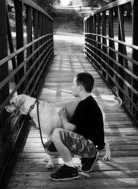 Side view of man with dog crouching on footbridge at park