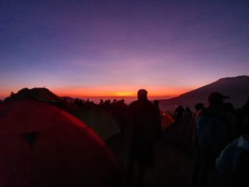 Silhouette people looking at mountains against sky during sunset