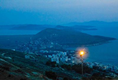 High angle view of illuminated city by sea against sky at dusk