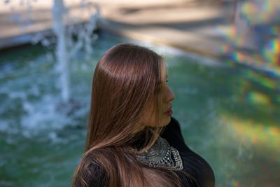 Young woman looking away against fountain