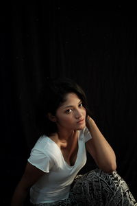 Portrait of young woman sitting against black background