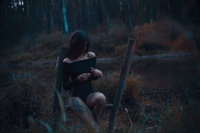 Woman sitting on built structure in forest