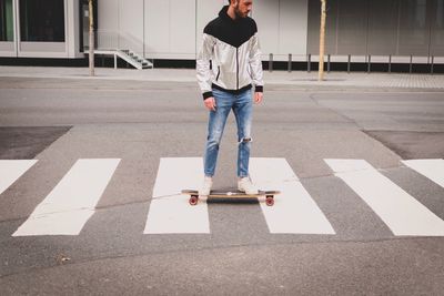 Full length of man standing on skateboard at road