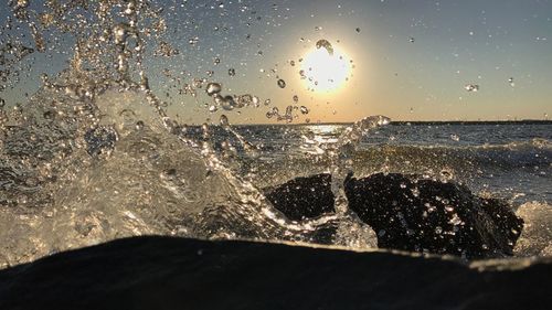 Close-up of water splashing on sea against sky during sunset