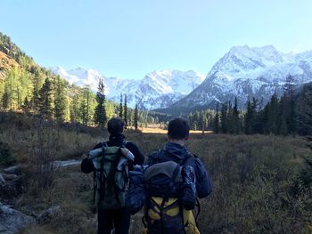 Rear view of male hikers looking at snowcapped mountains against blue sky