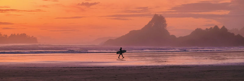 Silhouette woman walking on beach against sky during sunset