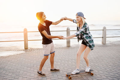 Full length of man teaching skating to girlfriend against sea