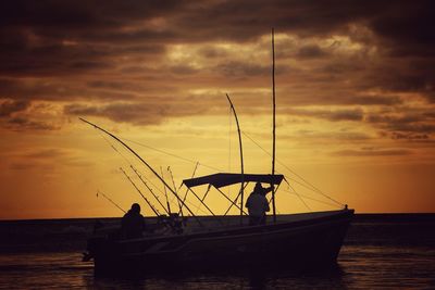 Silhouette men fishing in sea against sky during sunset