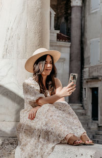 Beautiful happy young woman wearing long dress using mobile phone in city.