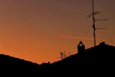 Low angle view of silhouette communications tower against sky during sunset