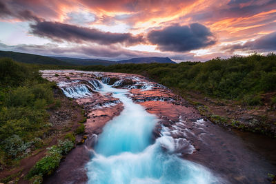 Scenic view of waterfall against sky during sunset