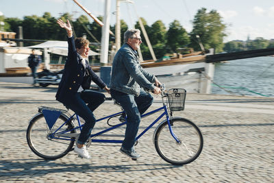 Full length side view of senior couple riding tandem bike on road in city during vacation