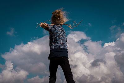 Low angle view of girl with dried plants walking against sky