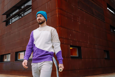 Young man holding skateboard walking on footpath