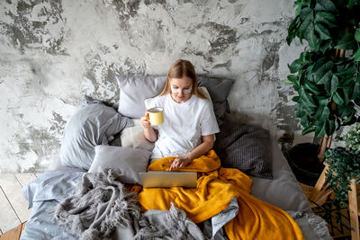 Side view of young woman sitting against wall