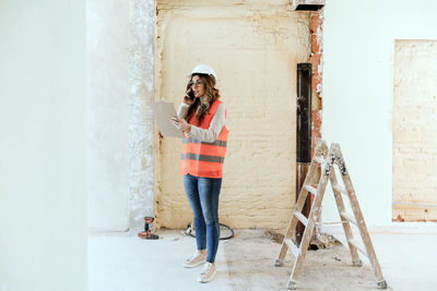 Architect woman in construction site talking on mobile phone and blueprints.home renovation