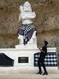 Full length of man standing by statue against wall