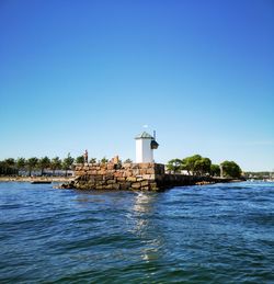 Lighthouse by sea against clear blue sky