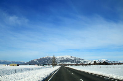 Road leading towards snowcapped mountains against sky