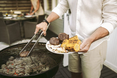 Midsection of mature man preparing barbecue meal in back yard