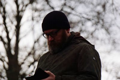 Man using phone while standing against tree