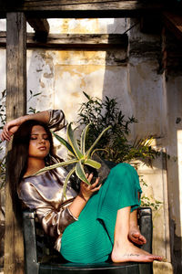 Young woman holding plant while sitting on chair