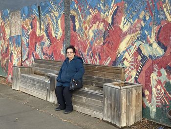 Full length portrait of senior woman sitting against graffiti wall