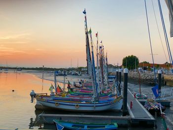 Fishing boats moored at harbor against sky during sunset