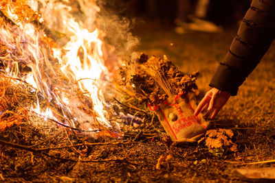 Cropped hand holding sack of plant by bonfire at night