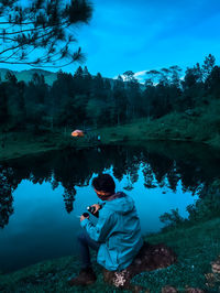 Rear view of men sitting by lake against trees