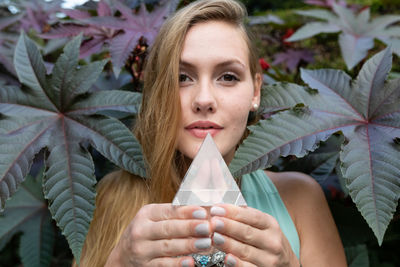 Portrait of young woman holding prism while standing against plant