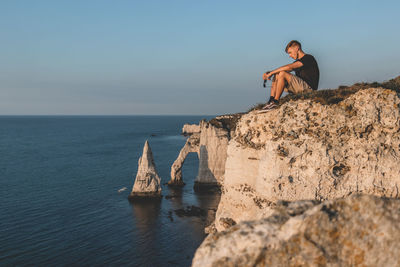 Young woman on rock by sea against sky