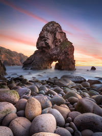 Rocks on sea shore against sky during sunset