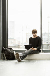 Young man using laptop while sitting on sill at railroad station