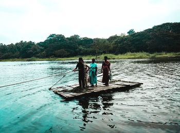 Rear view of men in boat on lake against sky