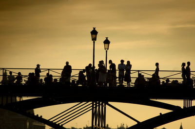 Silhouette people by railing against sky during sunset